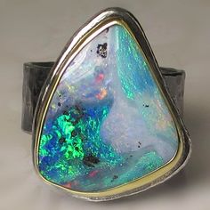 Stunningly gorgeous natural solid Australian boulder opal cabochon set in solid 18k gold bezel hammered sterling silver base. Hammered sterling silver band(approx. 8.3mm wide X 1mm thick). This gorgeous fiery opal measures 16.3 x 20 X 4mm deep and weighs 8.64cts.  All metal is from recycled sources. All silver has been oxidized and polished and will wear to an aged patina. This ring is a size 7 1/2 and I can stretch to a 7 3/4. Attractively boxed. Photos have been taken up close for detail. Please refer to dimensions. Custom rings are available. Convo me for information. INTERNATIONAL BUYERS: Insured first class(where applicable). Buyer is responsible for any customs taxes/fees. Luxury Hallmarked Silver Opal Ring, Blue Cabochon Opal Ring, Blue Opal Oval Cabochon Ring In Sterling Silver, Blue Cabochon Opal Ring In Sterling Silver, Boulder Opal Ring, Luxury Polished Opal Ring, Oval Cabochon, Ethiopian Opal Ring, Unusual Rings, Australian Boulder Opal