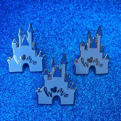 three disney castle pin badges sitting on top of a blue carpeted floor, with the word love written in front of them