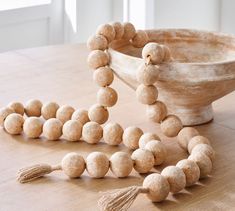 a wooden bead necklace with tassels on a table next to a bowl