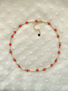 a red and green beaded necklace on a white cloth with flowers in the middle