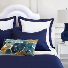 a bed with blue and white sheets, pillows and lamps on the nightstands next to it