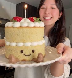 a woman holding a plate with a cake on it and a lit candle in the middle