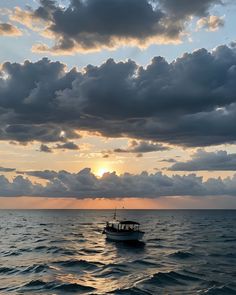 a small boat floating on top of the ocean under a cloudy sky with sun peeking through clouds