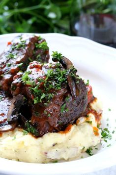 a white plate topped with mashed potatoes covered in meat and garnished with parsley