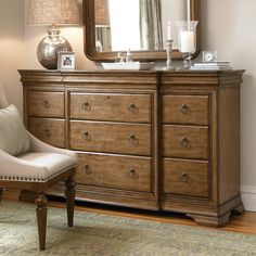 a dresser with a mirror, lamp and chair next to it in a living room