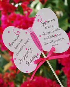 two butterfly shaped fans with pink ribbons on them in front of red and pink flowers