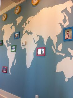 a world map is painted on the wall with several frames around it, and there are clocks