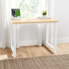 a white table with a book on it and a plant in the corner next to it