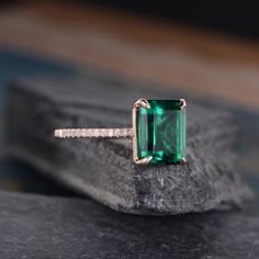 an emerald and diamond ring sitting on top of a rock