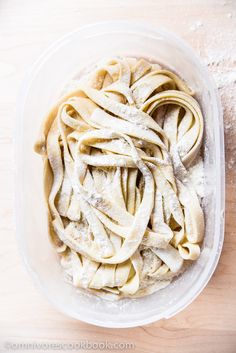 an uncooked pasta dish in a plastic container on a wooden table top with flour