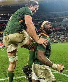 two rugby players in green and white uniforms are on the field with their arms around each other