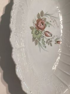 a white plate with flowers and leaves on the rim is sitting on a table next to a wall