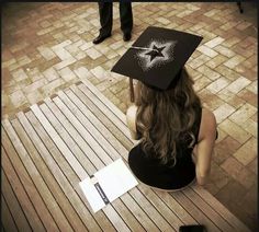 a woman sitting on top of a wooden bench wearing a black graduation cap with stars