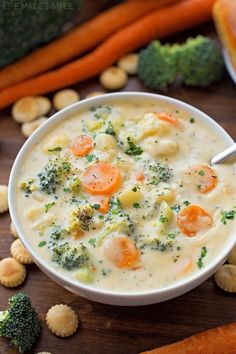 a bowl of soup with carrots, broccoli and crackers on the side