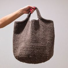 a hand holding a gray knitted bag over a white background with the handle extended