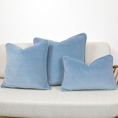 two blue pillows sitting on top of a white couch