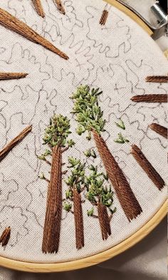 a close up of a embroidery on a table cloth with needles and trees in the middle