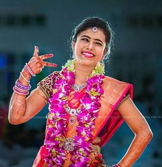 a woman dressed in pink and orange holding her hand up to the side while smiling