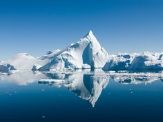 an iceberg in the middle of water surrounded by snow covered mountains and ice floes