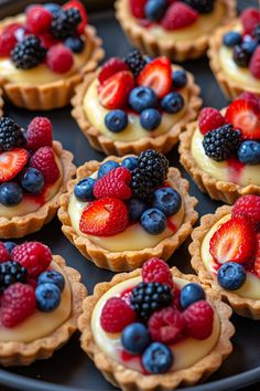 small tarts filled with fresh berries and blueberries on a tray for desserts