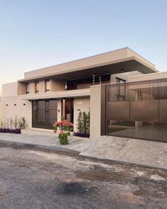 a modern house is shown with flowers in the foreground and an empty parking lot behind it