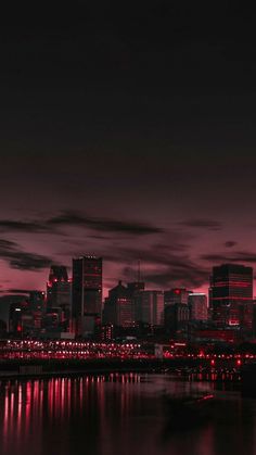 the city skyline is lit up at night with red lights and reflections in the water