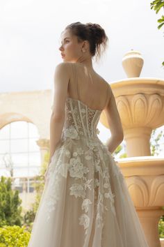 a woman in a wedding dress standing next to a fountain and looking off into the distance