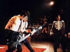 a man with no shirt on playing a guitar in front of other men wearing skeleton costumes