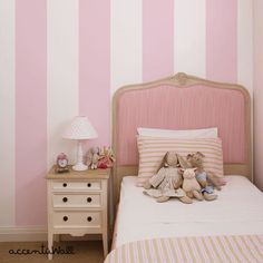 a pink and white striped wall in a child's bedroom with teddy bears on the bed