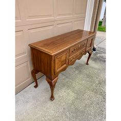 an old wooden desk sitting in front of a garage door next to a driveway with a cat laying on the floor