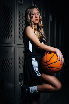 a beautiful young woman holding a basketball in front of lockers