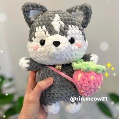 a hand holding a small gray and white crocheted cat with a flower in it's mouth