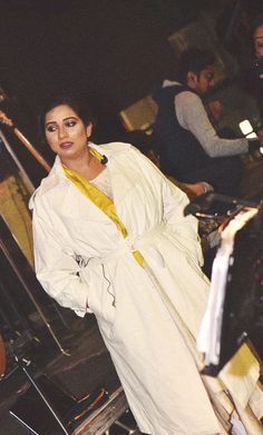 a woman in a white coat is standing on an escalator with people behind her