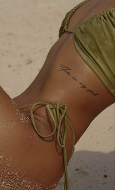 a woman with tattoos on her stomach laying in the sand