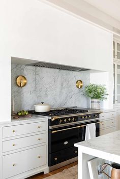 a kitchen with marble counter tops and gold accents on the stove top, along with white cabinets