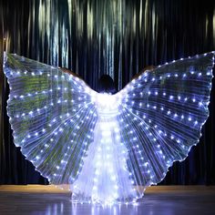 a woman is standing in front of a curtain with her wings spread out and lights on it