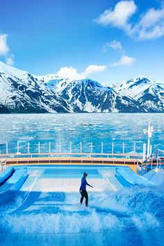 a man riding a wave machine on top of a blue water covered slope with mountains in the background