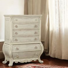 a white dresser sitting on top of a hard wood floor next to a curtained window