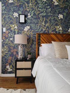 a bedroom with floral wallpaper and white bedding in front of a night stand