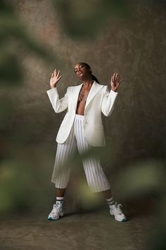 a woman in white jacket and pants standing with her hands out to the side while wearing tennis shoes