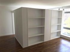 an empty room with white bookcases next to a window and hardwood flooring