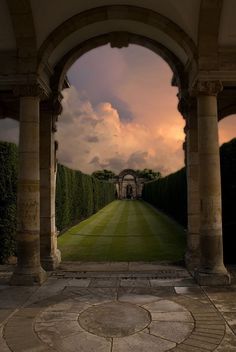 an archway leading into a lush green park with trees on either side and clouds in the sky