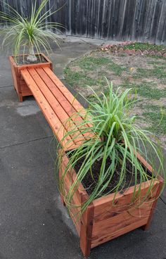 a wooden bench sitting next to a planter filled with potted plants on top of cement