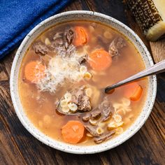 a bowl of soup with carrots, meat and cheese in it on a wooden table