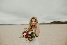 a woman standing in the desert holding a bouquet