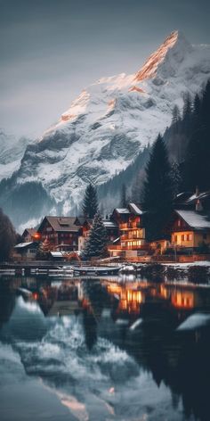 the mountains are covered in snow and lit up by lights on houses next to a body of water