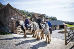 three people are riding horses on a path next to a stone building and fenced in area