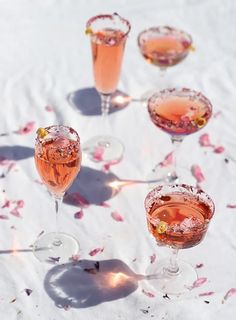 four glasses filled with pink liquid on top of a white table covered in rose petals