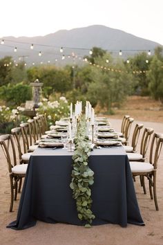 a long table is set up with candles and place settings for an outdoor dinner party