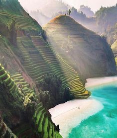 an aerial view of rice terraces on the side of a mountain with blue water below